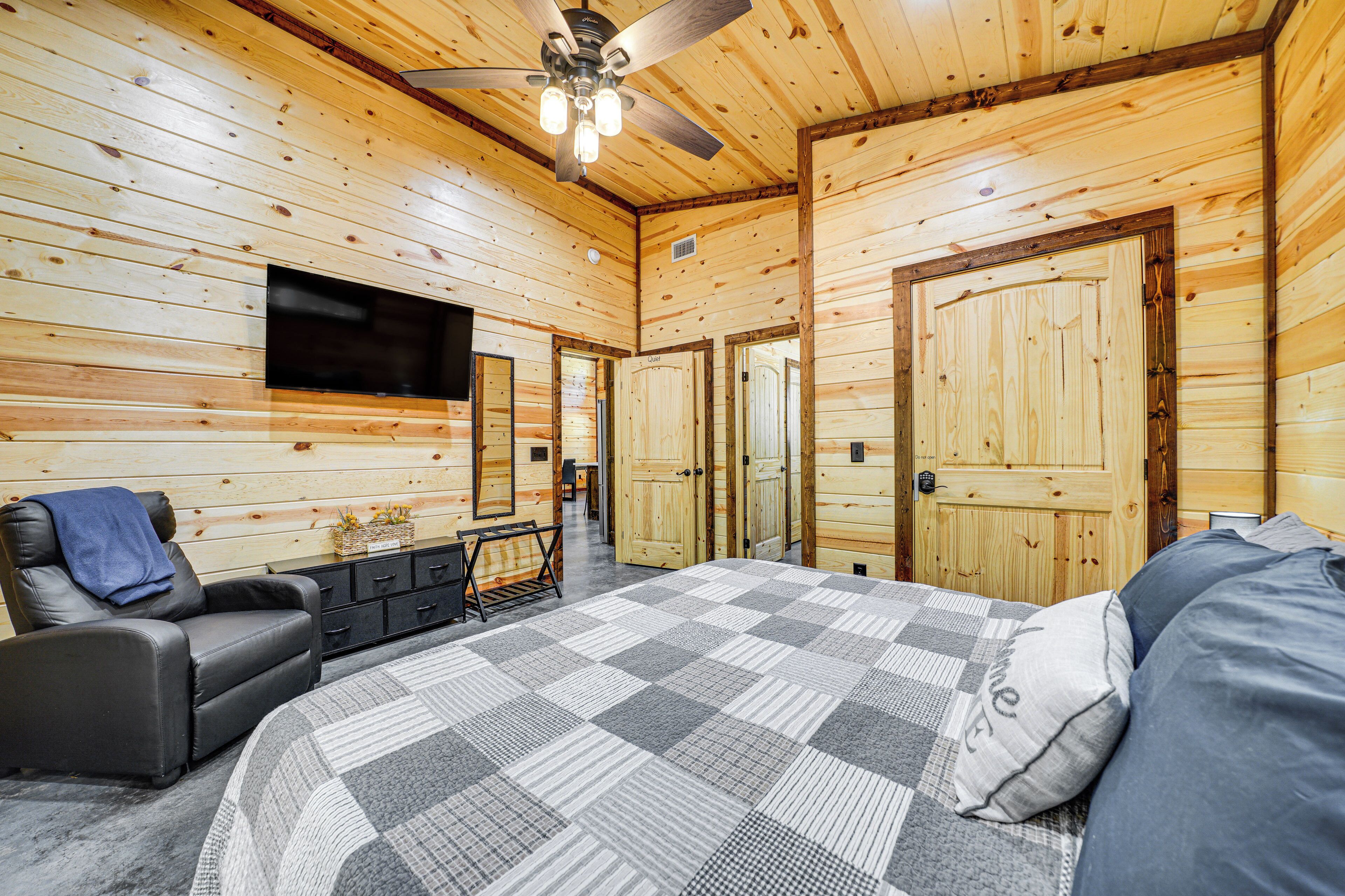 A wooden cabin bedroom with a bed, a chair, a TV, and a ceiling fan.