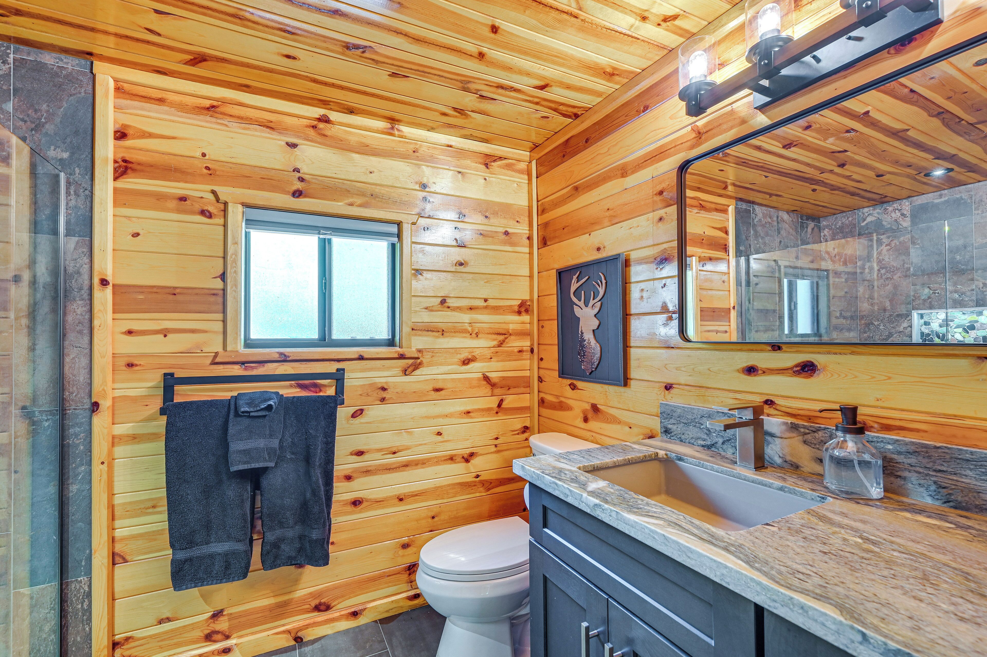 A wooden-paneled bathroom with a toilet, sink, and a window.