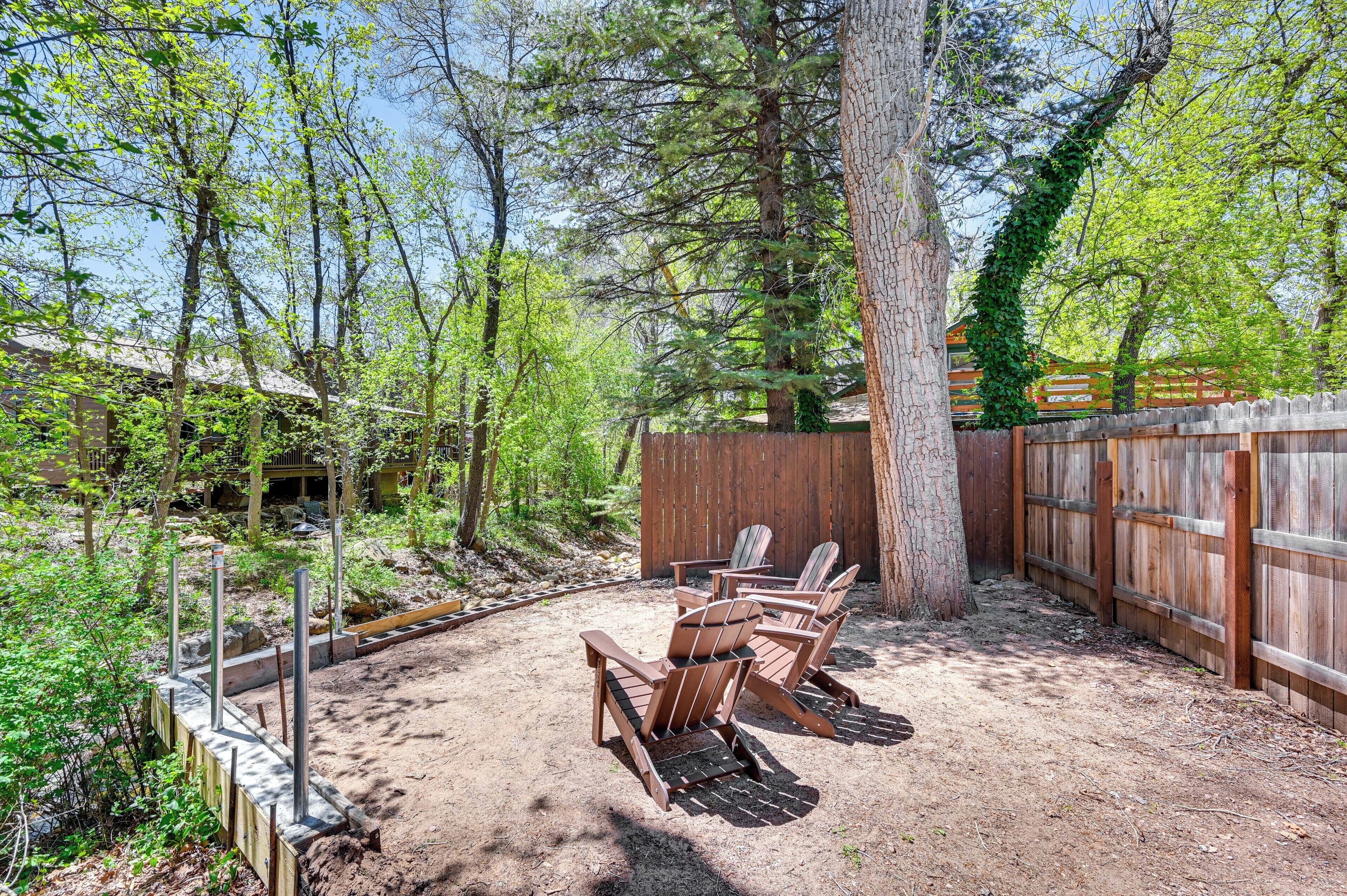 An outdoor seating area with Adirondack chairs, a wooden fence, and a tree.