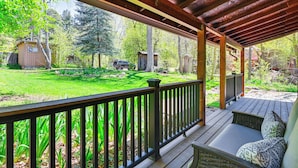 A covered porch with a view of a well-maintained backyard, including a lawn, trees, and a small shed.