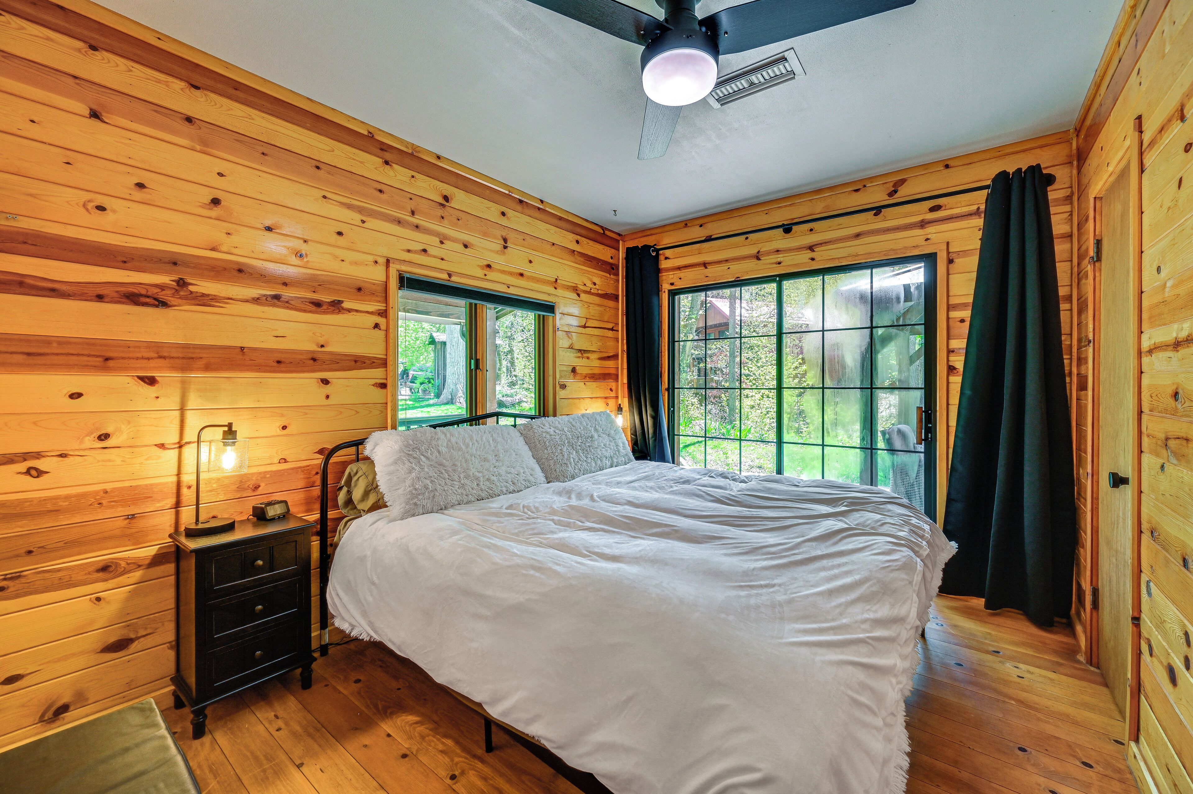 A wooden-paneled bedroom with a bed, nightstand, and windows.