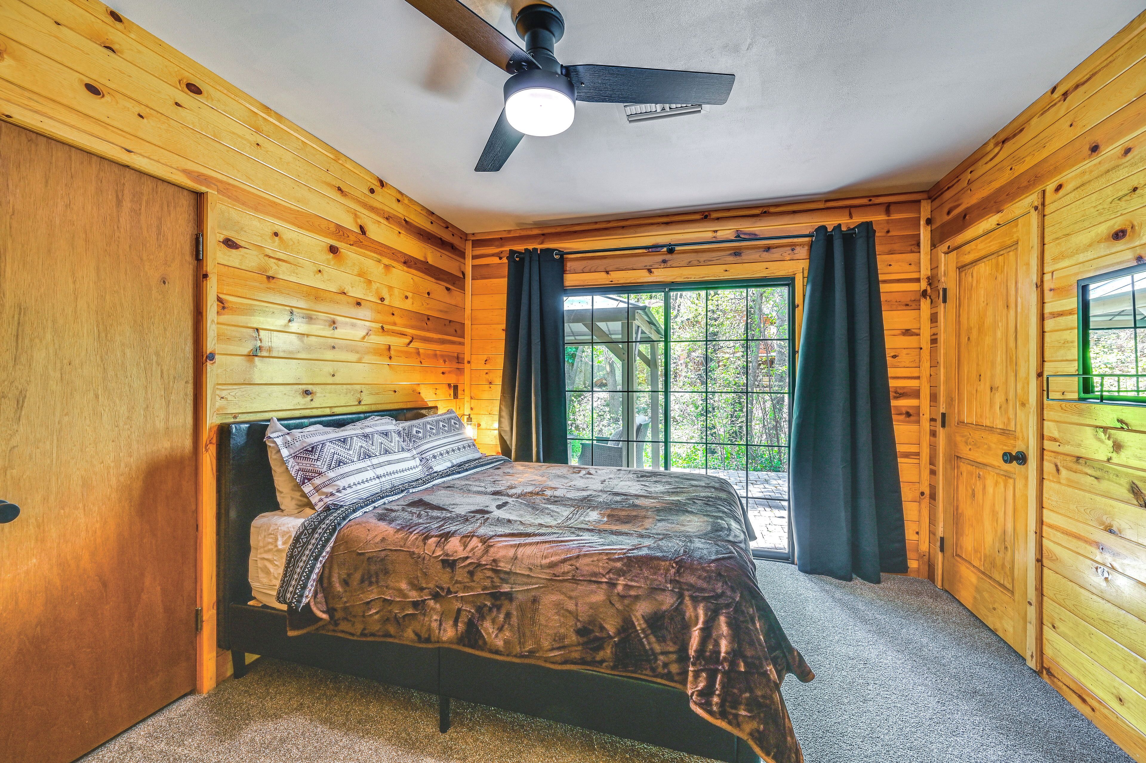 Dormitorio de cabaña de madera con cama, ventilador de techo y ventana con cortinas.