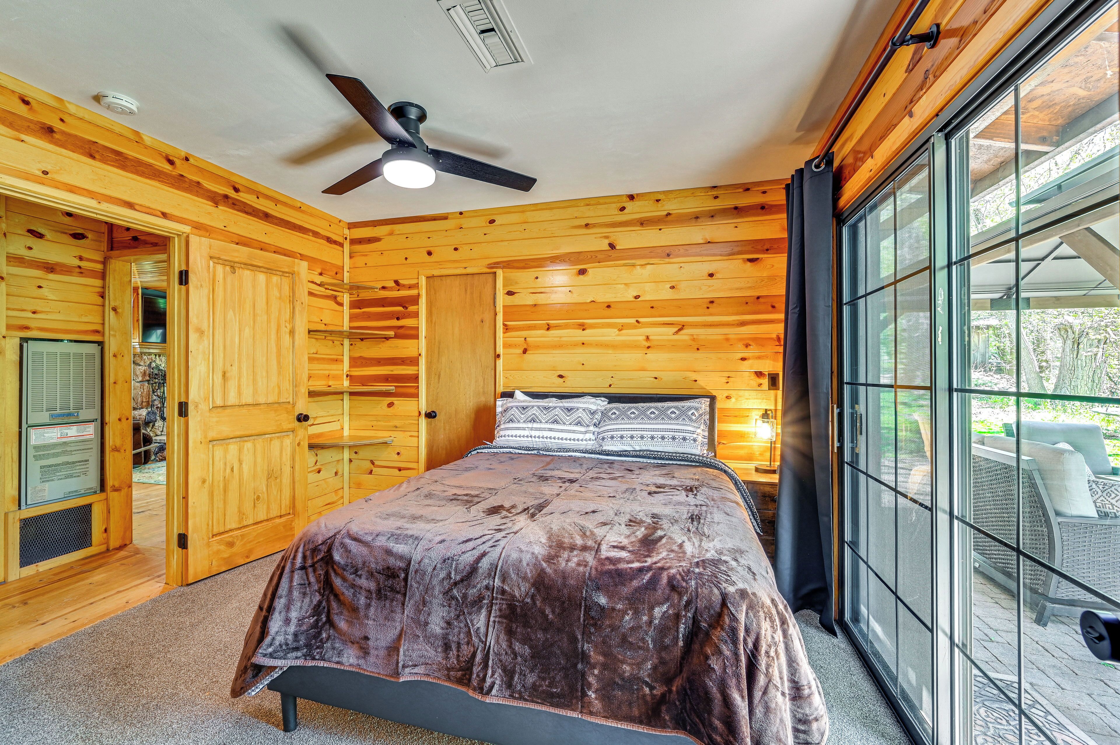 Ein Schlafzimmer einer Holzhütte mit Bett, Deckenventilator und großem Fenster.