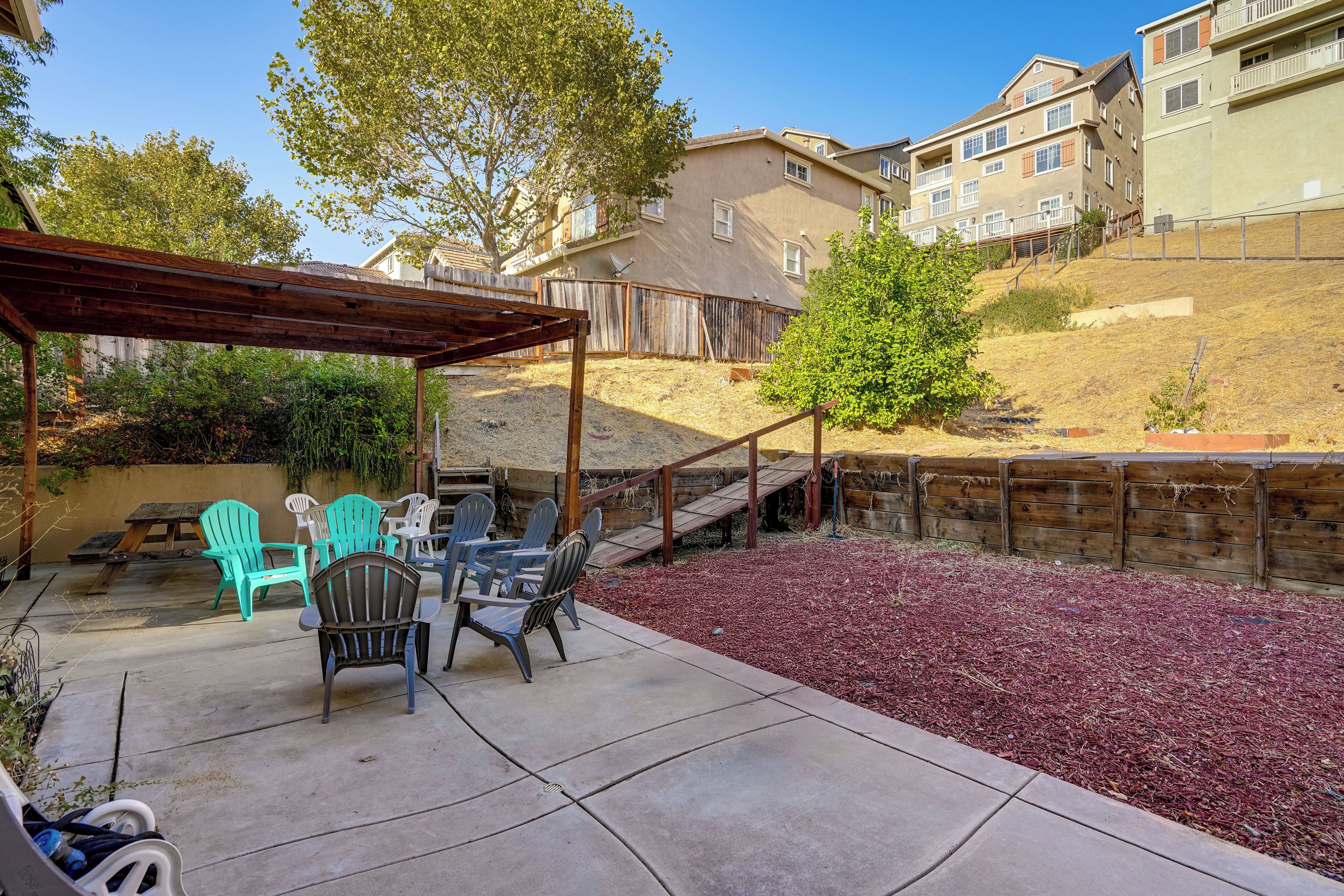 A patio area with outdoor furniture, a pergola, and a view of residential buildings in the background.