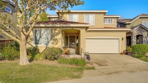 A two-story house with a front garage, a well-maintained lawn, and a tree in the front yard. - Spacious Bay Point Family Home w/ Private Yard! (Pittsburg)