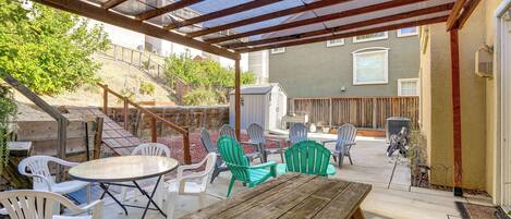 An outdoor patio with a wooden table and chairs, a covered seating area, and a view of a residential building in the background.