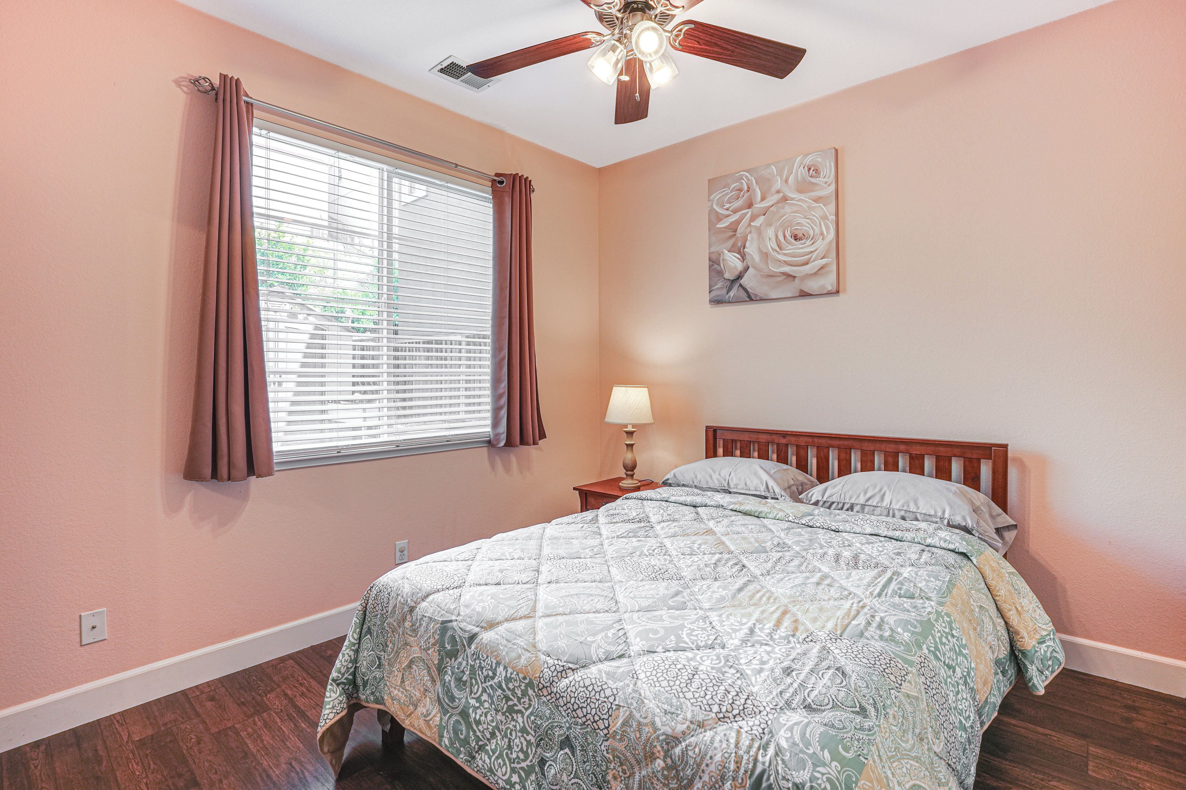 A bedroom with a bed, a nightstand, a ceiling fan, and a window with curtains.