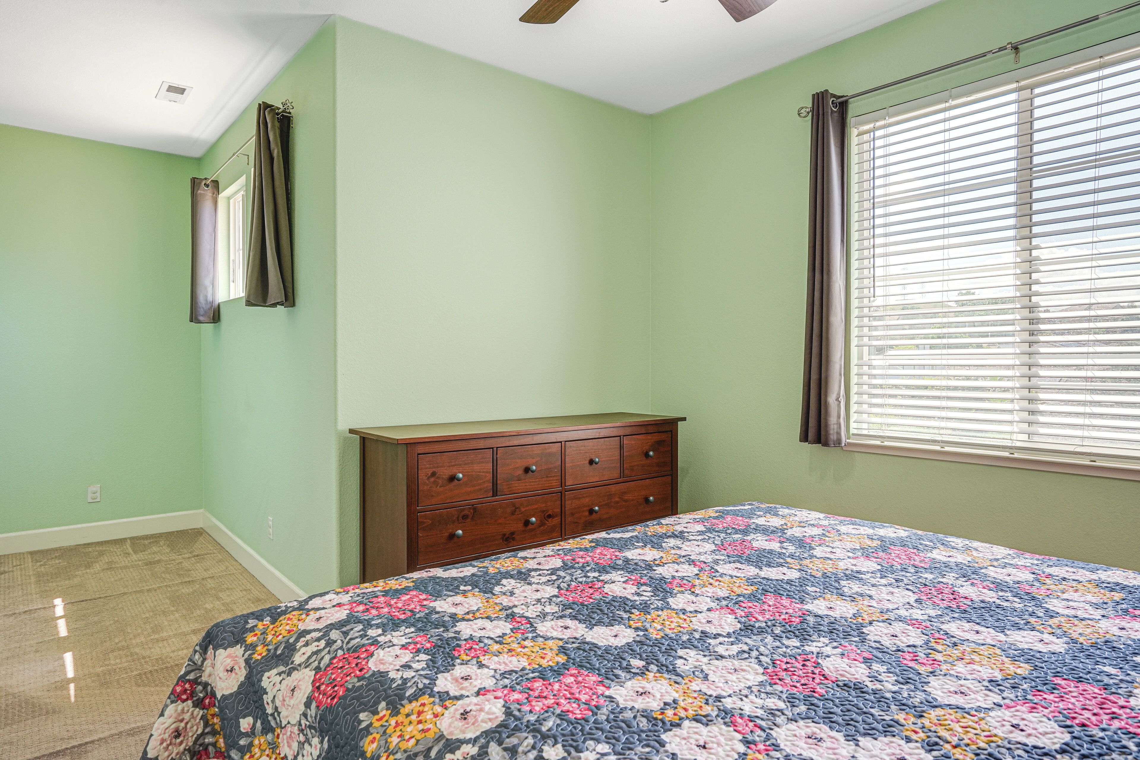 A bedroom with a bed, a dresser, a window with blinds, and a ceiling fan.
