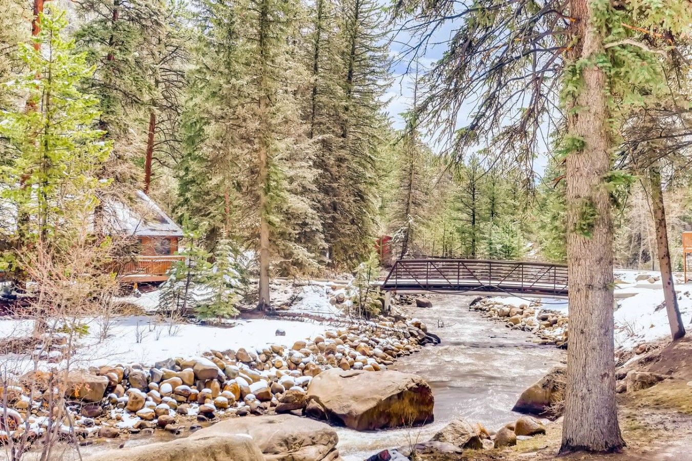 Une cabane dotée d’une terrasse en bois, entourée d’un paysage enneigé et d’arbres.