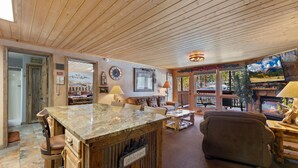 A cozy living area with a wooden ceiling, a stone fireplace, a television, and a comfortable seating area. - Quiet Fall River Escape • River Views • RMNP (Estes Park)
