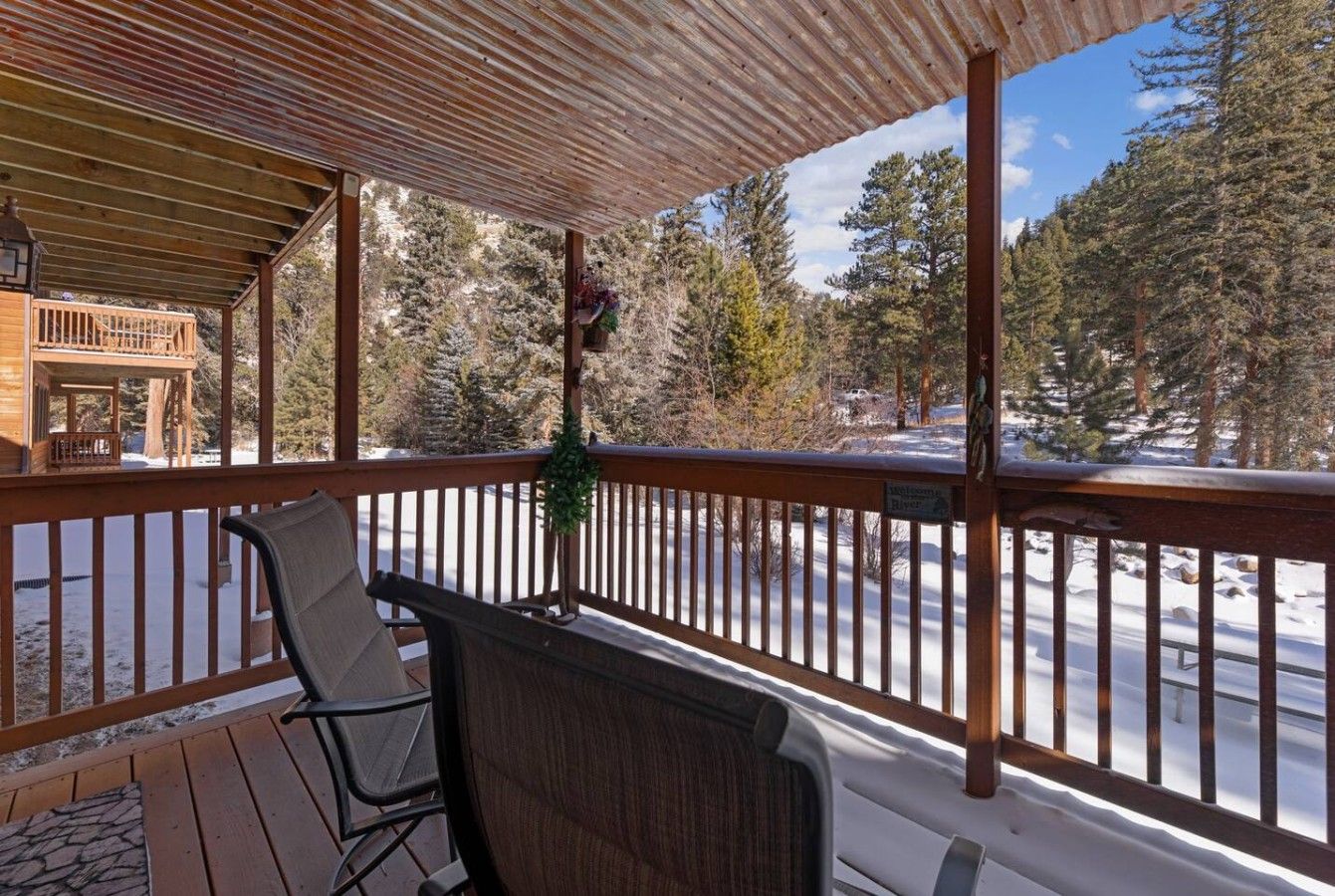 A covered outdoor area with a wooden deck, a chair, and a railing overlooking a snowy landscape.