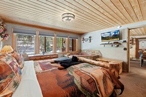 A cozy room with a large bed, a stone fireplace, a television, and a view of the outdoors.