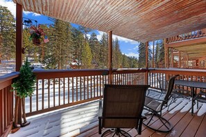 A wooden deck with a bench and chairs, overlooking a snowy landscape with trees.
