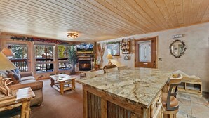 A cozy living room with a large wooden ceiling, a stone island, and a fireplace. - Quiet Fall River Escape • River Views • RMNP (Estes Park)