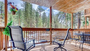 A wooden deck with two chairs and a table, overlooking a forested area. - Quiet Fall River Escape • River Views • RMNP (Estes Park)