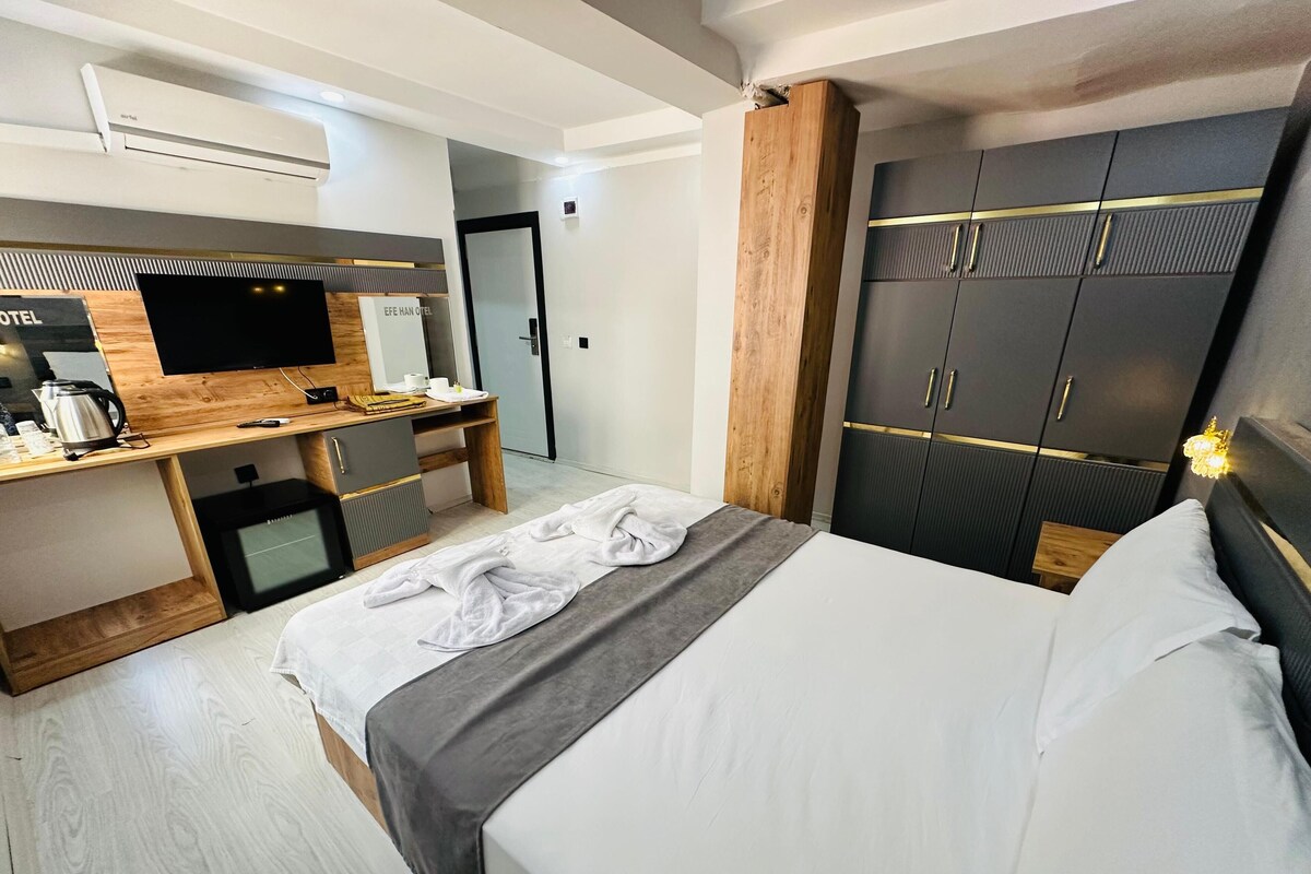 Habitación de hotel con cama, escritorio con televisor de pantalla plana, cafetera y armario con espejo.