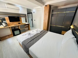 Habitación de hotel con cama, escritorio con televisor de pantalla plana, cafetera y armario con espejo.
