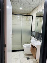 Un baño moderno con mampara de vidrio, inodoro blanco y tocador con espejo.