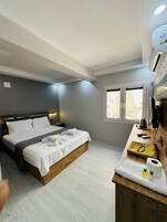 Una habitación de hotel moderna con una cama de madera, un pequeño escritorio con una tetera y una ventana con vistas.