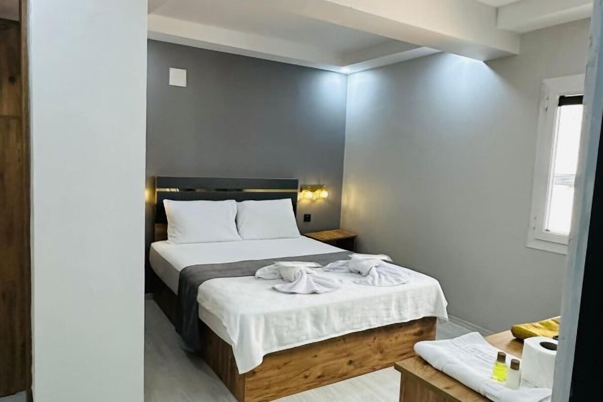 Una cama bien hecha con sábanas y toallas blancas, un cabecero de madera y una mesita de noche con una lámpara y una botella.