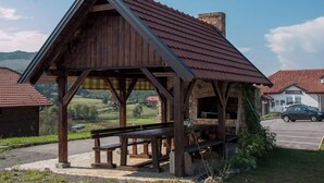 A wooden pavilion with a sloped roof, benches, and a stone fireplace. - Apartments Ivanka (Rakovica)
