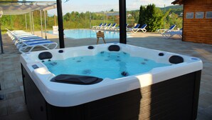 A hot tub with a pool in the background, lounge chairs, and a wooden cabin. - Apartments Ivanka (Rakovica)