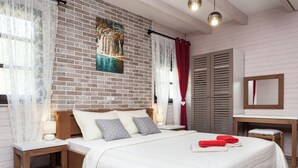 A bedroom with a brick wall, a bed with white bedding, a nightstand, a wooden chair, and a painting. - Apartments Ivanka (Rakovica)