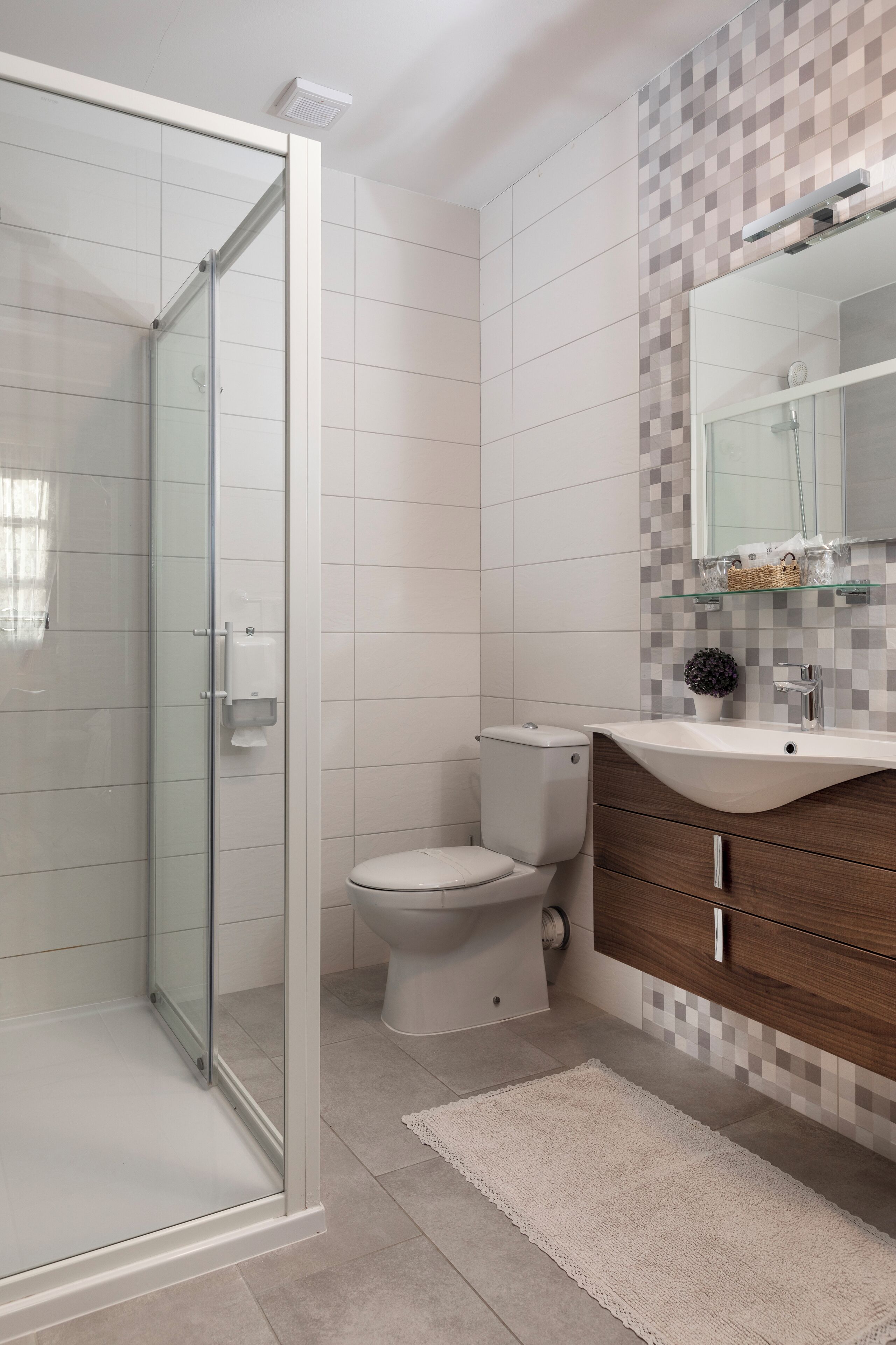 Um banheiro moderno com box de vidro, vaso sanitário, toucador com espelho e painel de azulejos.