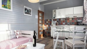 A modern kitchen with white cabinets, a glass dining table, and a seating area with a sofa and chairs. - Apartments Ivanka (Rakovica)