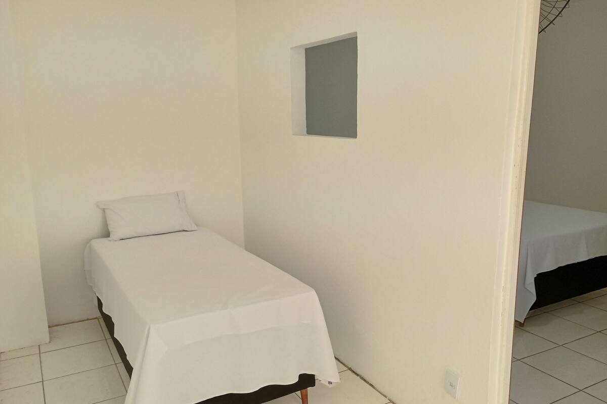 Habitació petita amb un llit individual, una llitera blanca, una finestra petita i un paviment de rajoles.