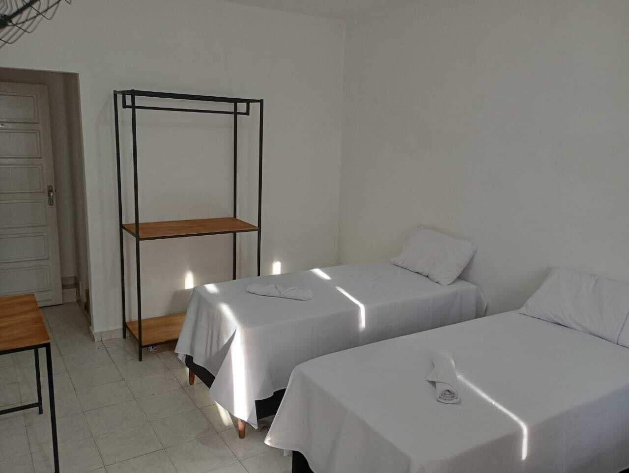 Een hotelkamer met twee eenpersoonsbedden, een houten plankunit en een klein tafeltje.