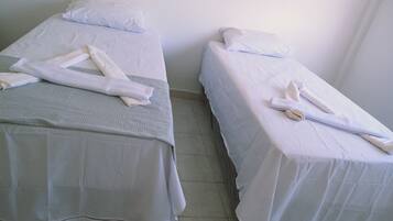 Two single beds with white linens and towels, a tiled floor, and plain walls.