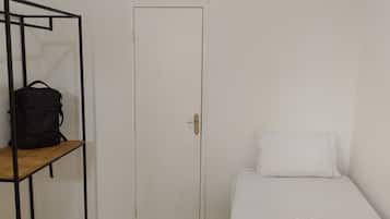A room with a bed, a white door, and a black backpack on a shelf.