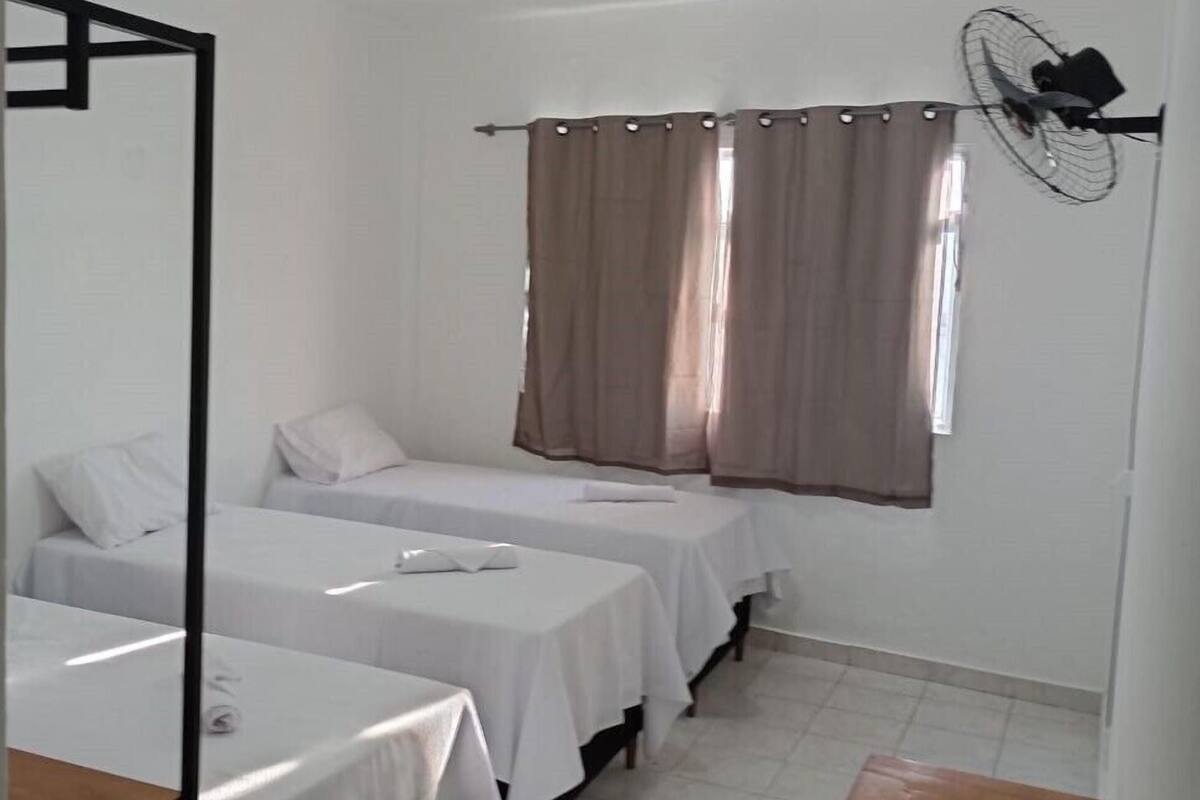 Habitació amb dos llits individuals, una taula petita, un ventilador i una finestra amb cortines.