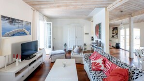 Un salón amplio con televisor, muebles blancos y un ventanal grande.