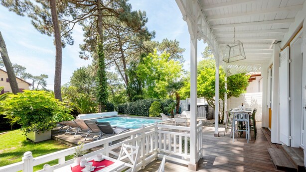 Una terraza de madera con mobiliario exterior, piscina y abundante vegetación.