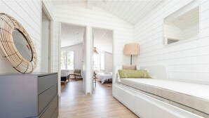Una habitación moderna y bien iluminada, con suelo de madera, un sofá blanco con cojines, un espejo grande y una cesta de mimbre sobre un mueble gris.