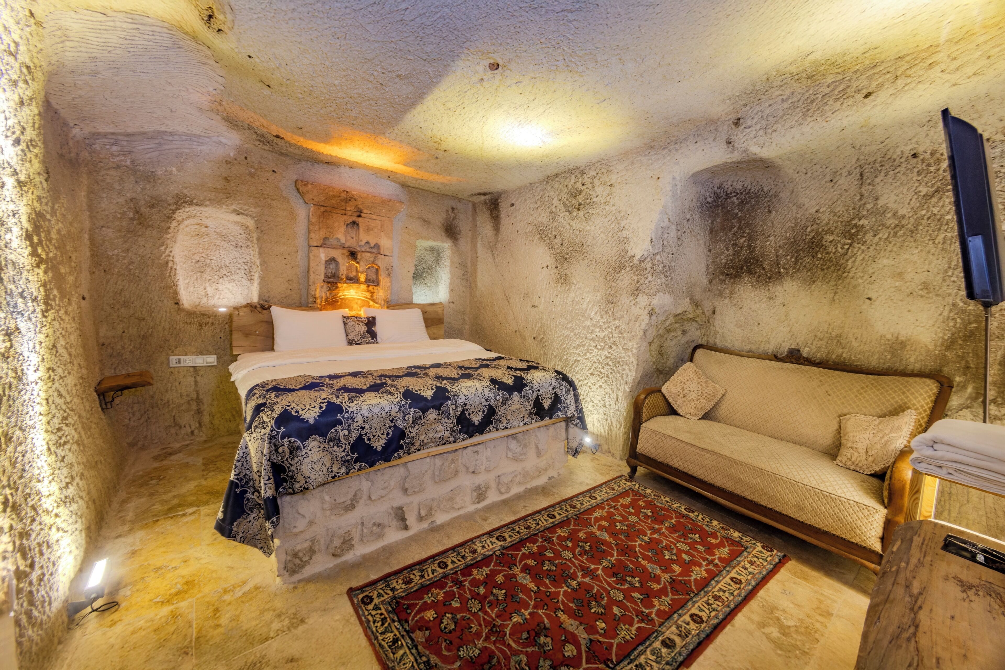 A room with a bed, a sofa, a rug, and a wall-mounted TV.