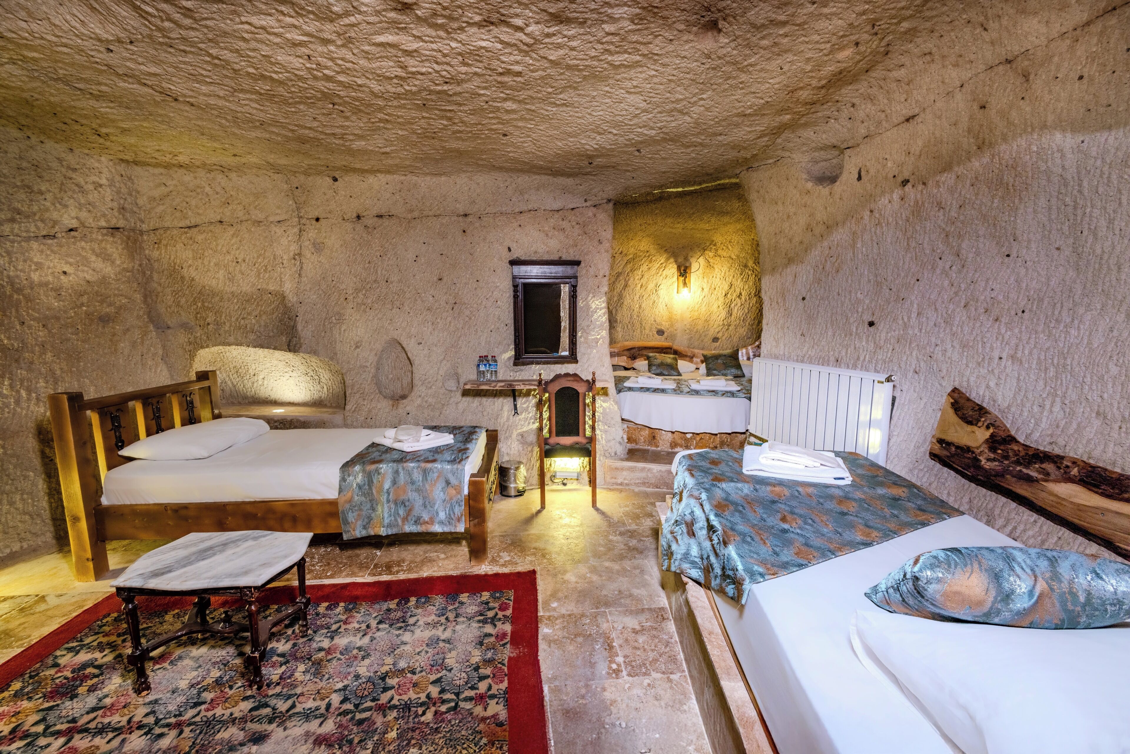 A rustic room with two wooden beds, a small table, a chair, and a window with a mirror.