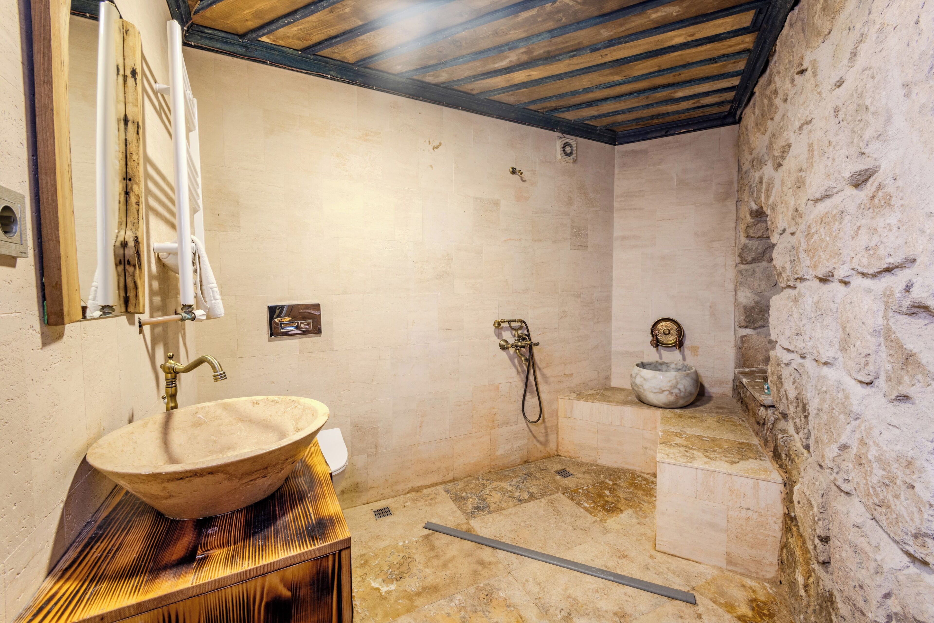 A bathroom with a stone sink, a shower, and a stone wall.