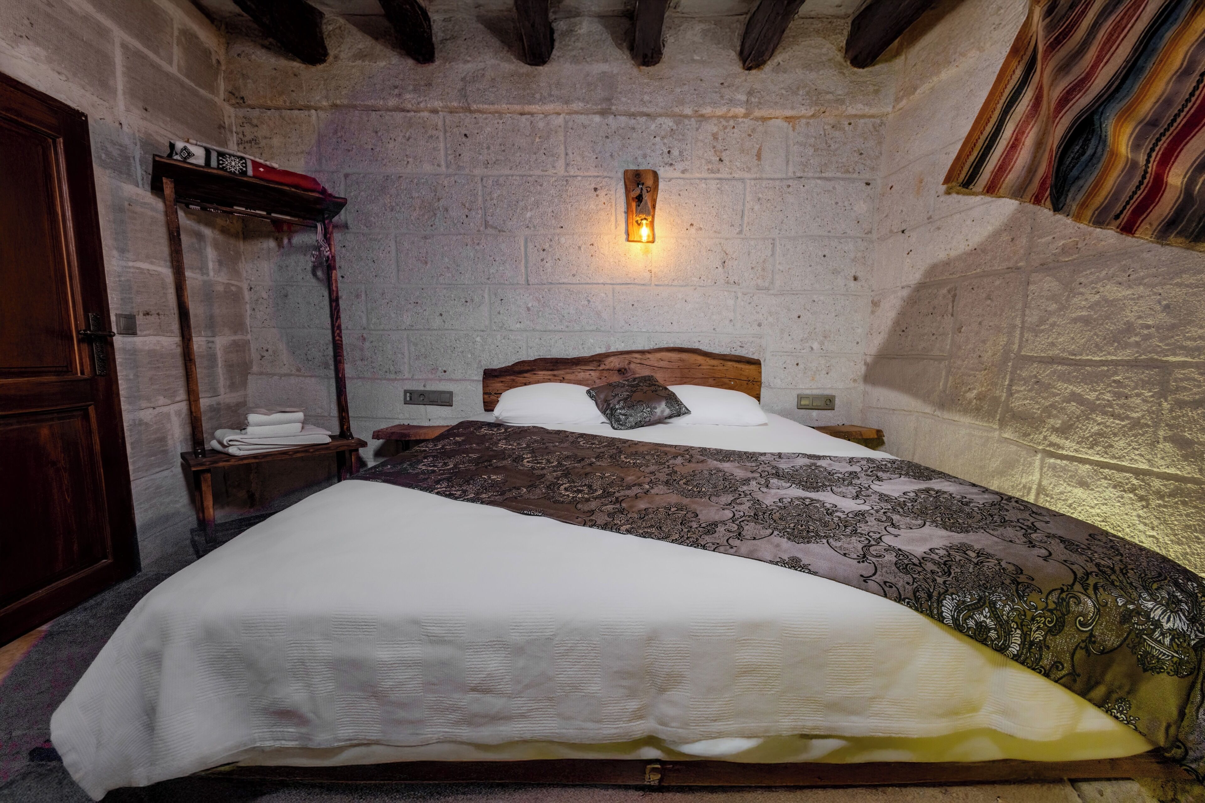 Un dormitorio con cama de madera, una mesita de noche, una lámpara de pared y una pared de piedra.