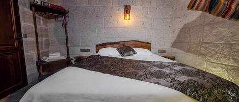 Un dormitorio con cama de madera, una mesita de noche, una lámpara de pared y una pared de piedra.