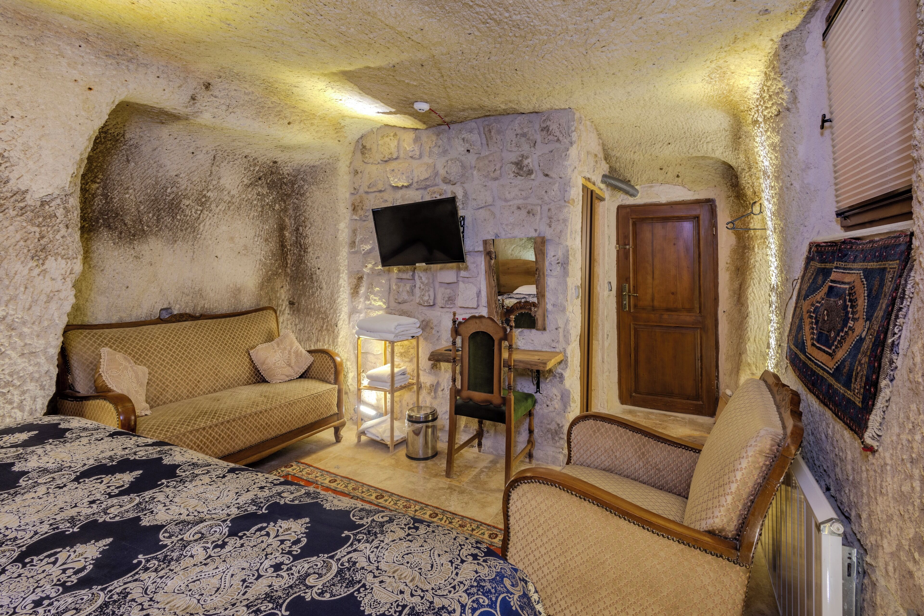 A room with a bed, two sofas, a small table, a chair, a television, and a door.