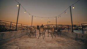 A rooftop terrace with chairs and string lights against a sunset backdrop.