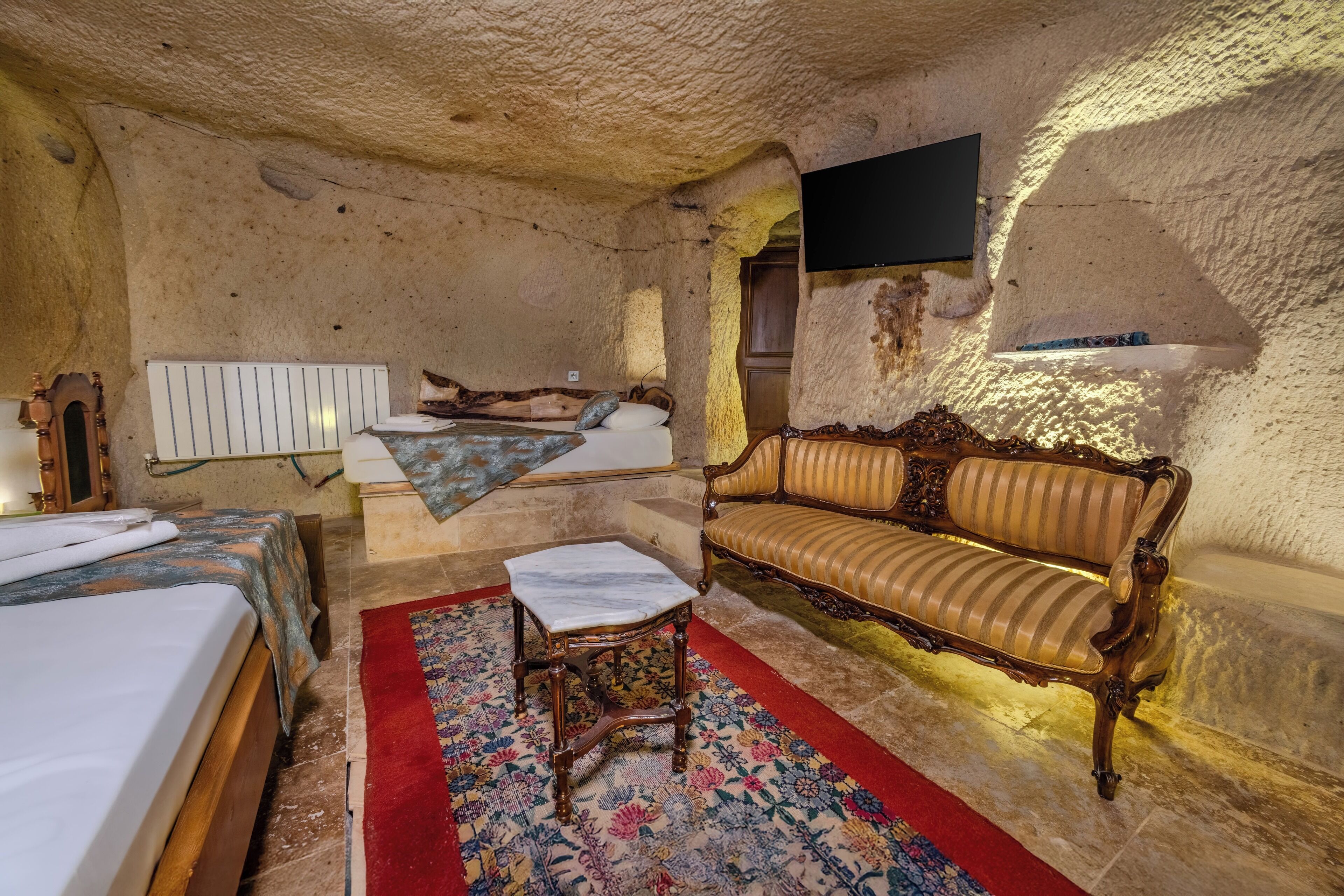 A room with a bed, a sofa, a small table, and a television mounted on the wall.