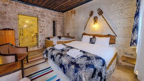 A bedroom with a stone wall, wooden ceiling beams, a large bed, a wooden chair, a bathtub, and a small wooden shelf.