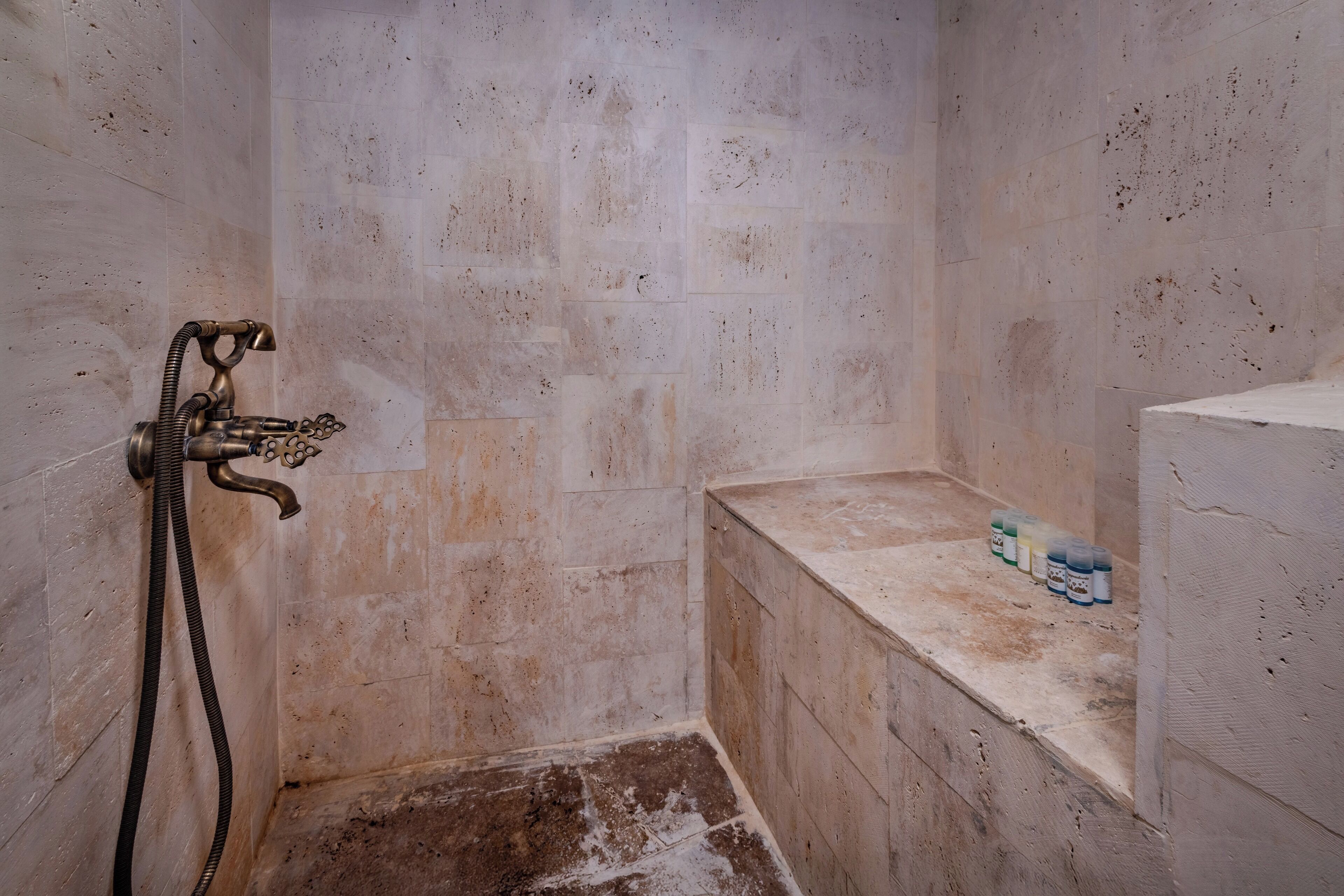 A small, tiled shower area with a handheld showerhead and a bench.