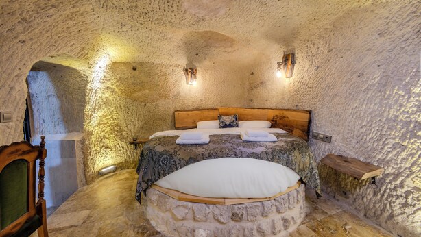 A cozy, stone-walled bedroom with a large bed, two bedside tables, and a wooden chair.