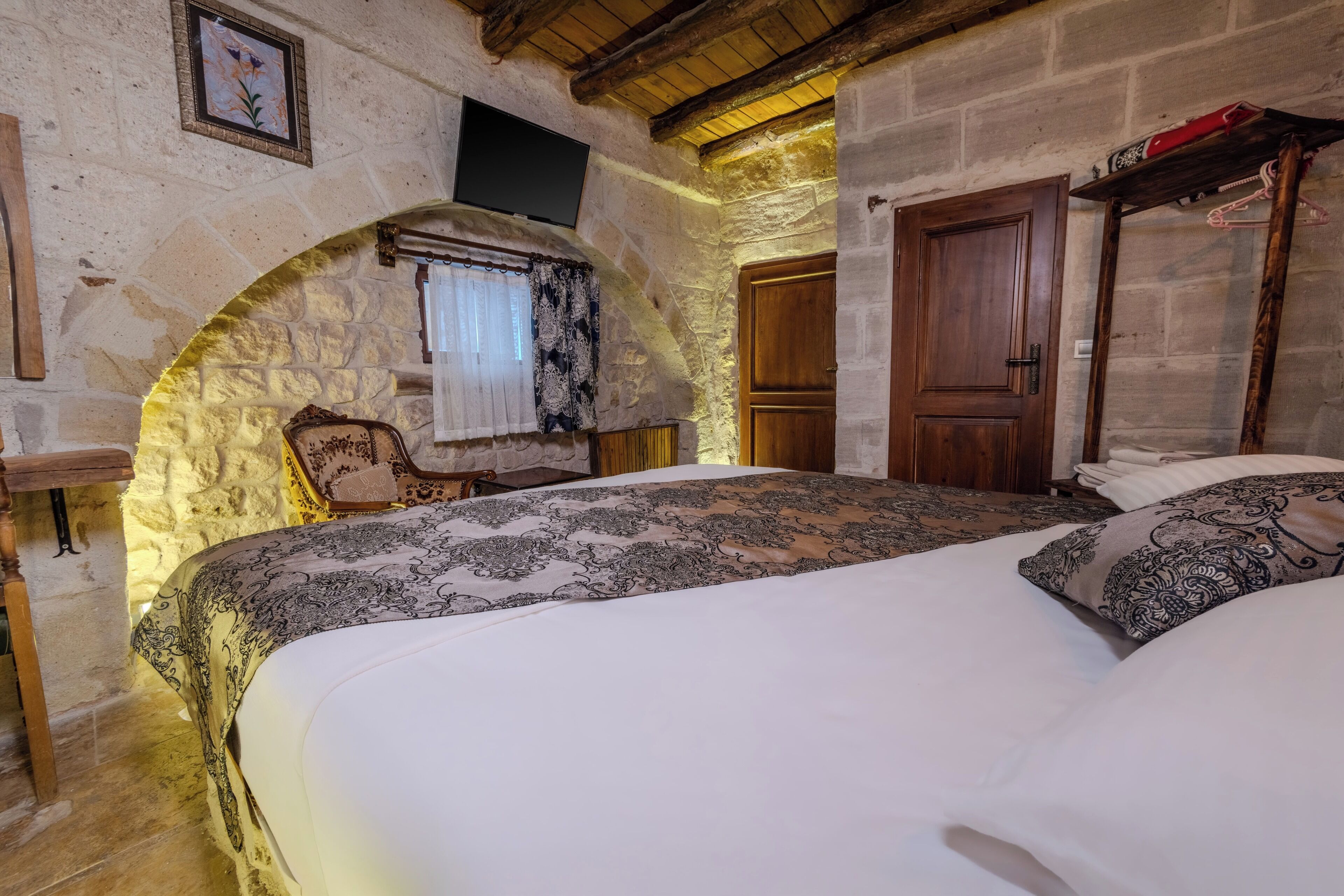 Une chambre avec un mur en pierre, une porte en bois et un lit recouvert d’une literie à motifs.
