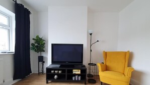Un salon avec un meuble de rangement noir pour les appareils électroniques, un fauteuil jaune, une plante en pot et un lampadaire.